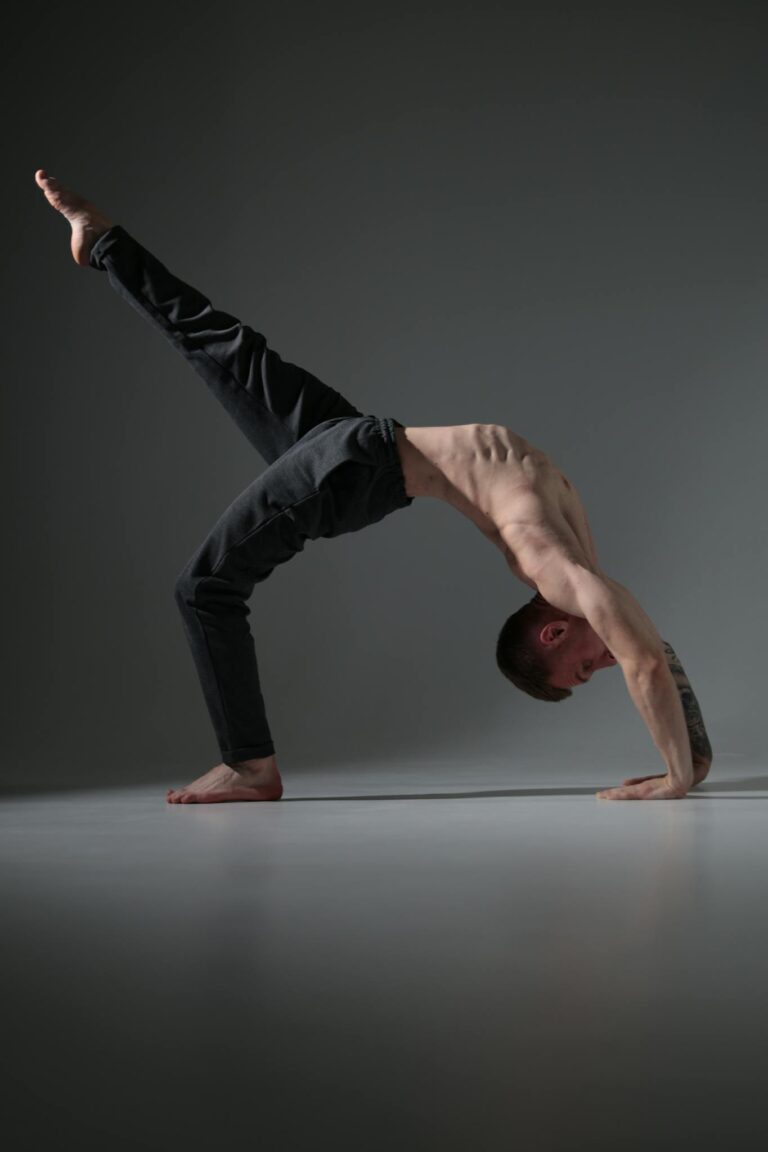 A fit man executes a yoga pose in a dimly lit studio, showcasing strength and balance.
