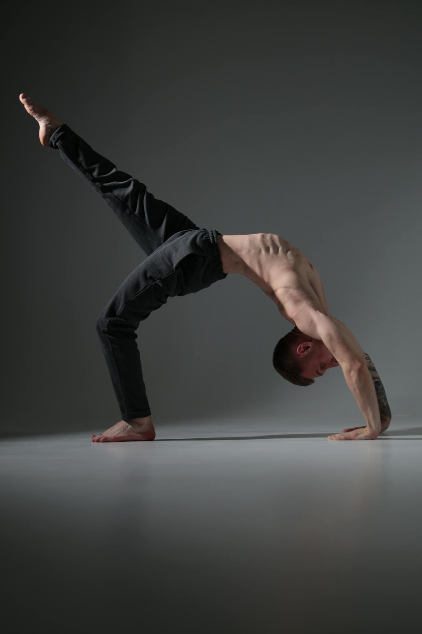 A fit man executes a yoga pose in a dimly lit studio, showcasing strength and balance.